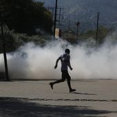 A man runs for cover as riot police launch tear gas in an effort to remove street vendors in the Champs de Mars area, next to the National Palace, in Port-au-Prince, Haiti, Tuesday, April 2, 2024. (AP Photo/Odelyn Joseph)