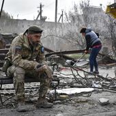 A Ukrainian serviceman smokes sitting on a bench as a local resident clears debris near a building damaged in the Russian air raid in the town of Orikhiv, Zaporizhzhia region, Ukraine, Friday, Apr. 5, 2024. (AP Photo/Andriy Andriyenko)