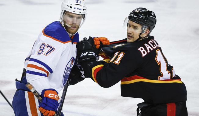 Edmonton Oilers forward Connor McDavid (97) holds the jersey of Calgary Flames forward Mikael Backlund (11) during the third period of an NHL hockey game Saturday, April 6, 2024, in Calgary, Alberta. (Jeff McIntosh/The Canadian Press via AP)