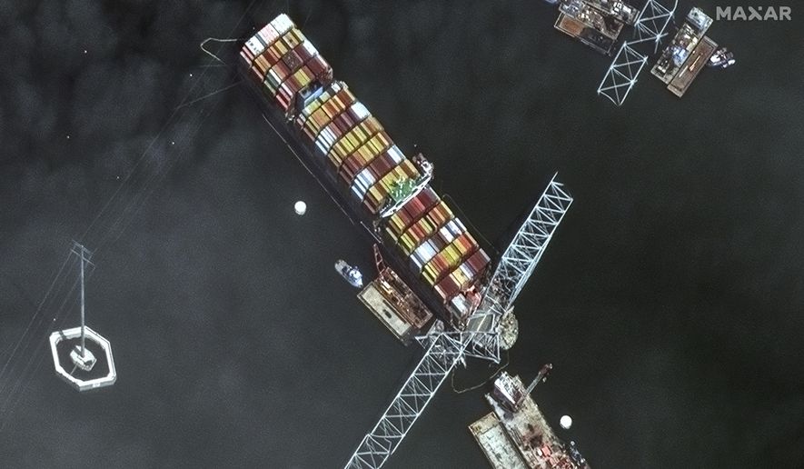This satellite image provided by Maxar shows the bow of the container ship Dali remains stuck underneath sections of the fallen Francis Scott Key Bridge, while salvage crews and barges with cranes continue removing some of the bridge debris and hundreds of shipping containers still onboard the vessel, in Baltimore, Monday, April 8, 2024. (Satellite image 2024 Maxar Technologies via AP)