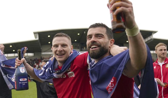 Wrexham&#x27;s Paul Mullin and Elliot Lee on the pitch celebrating promotion to League One after the final whistle of the Sky Bet League Two match at the SToK Cae Ras, Wrexham, Saturday April 13, 2024. (Jacob King/PA via AP)