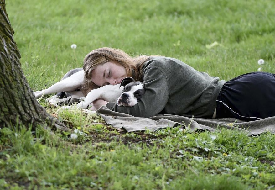 A woman and her dog nap between rain showers at Schenley Park, Tuesday, May 4, 2021, in Pittsburgh. A Gallup survey, released Monday, April 15, 2024, says that a majority of Americans say they would feel better if they could have more sleep. But in the U.S., where the ethos of grinding and pulling yourself up by your own bootstraps is ubiquitous, getting enough sleep can seem like a dream. (Pam Panchak/Pittsburgh Post-Gazette via AP, File)