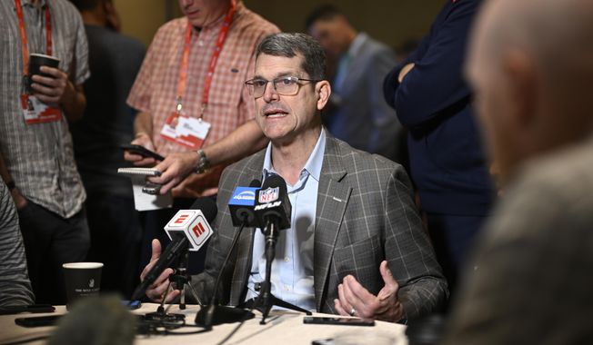 Los Angeles Chargers head coach Jim Harbaugh, center, talks with reporters during an AFC coaches availability at the NFL football owners meetings, Monday, March 25, 2024, in Orlando, Fla. Michigan was given three years of probation, fined and hit with recruiting limits by the NCAA on Tuesday, April 16, after football coaches and staff had impermissible contact with recruits and players under coach Jim Harbaugh while access was restricted during the COVID-19 pandemic.(AP Photo/Phelan M. Ebenhack, File)