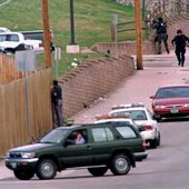 SWAT members run down Pierce Street while a Jefferson County, Colo., Sheriff&#x27;s Department deputy peers through a fence to keep an eye on Columbine High School after a pair of gunmen went on a shooting rampage inside the facility Tuesday, April 20, 1999, in the southwest Denver suburb of Littleton, Colo. (AP Photo/David Zalubowski, File)