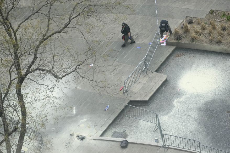 New York Police officers inspect a backpack left at the scene where a man lit himself on fire in a park outside Manhattan criminal court, Friday, April 19, 2024, in New York. Emergency crews rushed away a person on a stretcher after fire was extinguished outside the Manhattan courthouse where jury selection was taking place in former President Donald Trump's hush money criminal case. (AP Photo/Mary Altaffer)