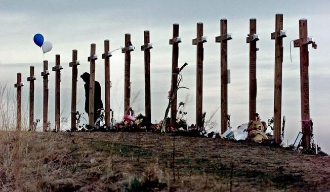 FILE - A woman stands among crosses posted on a hill above Columbine High School in Littleton, Colo., in remembrance of the people who died during a school shooting on April 20, 1999. Twenty-five years later, The Associated Press is republishing this story about the attack, the product of reporting from more than a dozen AP journalists who conducted interviews in the hours after it happened. The article first appeared on April 22, 1999. (AP Photo/Eric Gay, File)