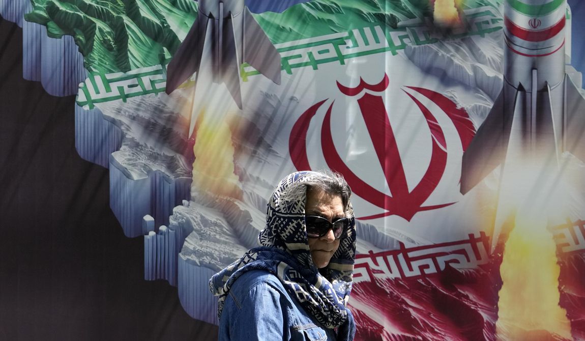 A woman walks past a banner showing missiles being launched from Iranian map in northern Tehran, Iran, Friday, April 19, 2024. Iran fired air defenses at a major air base and a nuclear site near the central city of Isfahan after spotting drones early Friday morning, raising fears of a possible Israeli strike in retaliation for Tehran&#x27;s unprecedented drone-and-missile assault on the country.(AP Photo/Vahid Salemi)