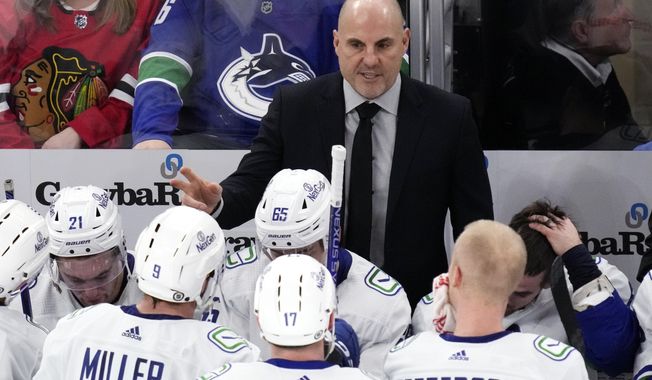 Vancouver Canucks head coach Rick Tocchet, top, talks to players during the third period of an NHL hockey game against the Chicago Blackhawks in Chicago, Sunday, Dec. 17, 2023. The Canucks won 4-3. In completing his first full season behind the Canucks bench, Tocchet is not alone among his coaching contemporaries in providing their respective teams a spark. Of the 16 teams entering the NHL playoffs this weekend, seven feature coaches who are in their first full year or hired as midseason replacements.(AP Photo/Nam Y. Huh)