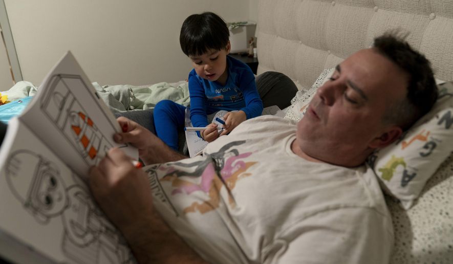 Scott Quinn and his 4-year-old son, Ethan, work on coloring books in a bed in Concord, Calif., Wednesday, Nov. 1, 2023. Ethan&#x27;s parents are among those who have opted for a private daycare instead of a free “transitional kindergarten.” Quinn said he has been discouraged to see Ethan — one of the oldest kids in his daycare class — pick up the behavior of kids who are several years younger than him. “In retrospect, it would have been better to send him to school to be around kids his age and older,” he said. (AP Photo/Jae C. Hong)