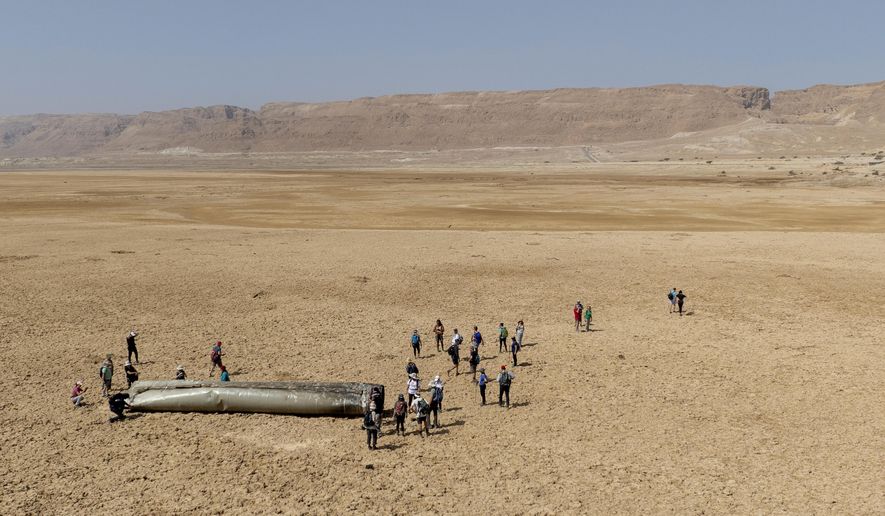 People gather around a component from an intercepted ballistic missile that fell near the Dead Sea in Israel, Saturday, April 20, 2024. Open fighting between Israel and Iran began April 1 with the suspected Israeli killing of Iranian generals at an Iranian diplomatic compound in Syria. That prompted Iran's retaliatory barrage last weekend of more than 300 missiles and drones that the U.S., Israel and regional and international partners helped bat down without significant damage in Israel. And then came Friday's strikes that hit near military and nuclear targets in Iran. (AP Photo/Itamar Grinberg)