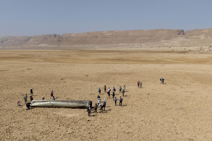 People gather around a component from an intercepted ballistic missile that fell near the Dead Sea in Israel, Saturday, April 20, 2024. Open fighting between Israel and Iran began April 1 with the suspected Israeli killing of Iranian generals at an Iranian diplomatic compound in Syria. That prompted Iran's retaliatory barrage last weekend of more than 300 missiles and drones that the U.S., Israel and regional and international partners helped bat down without significant damage in Israel. And then came Friday's strikes that hit near military and nuclear targets in Iran. (AP Photo/Itamar Grinberg)