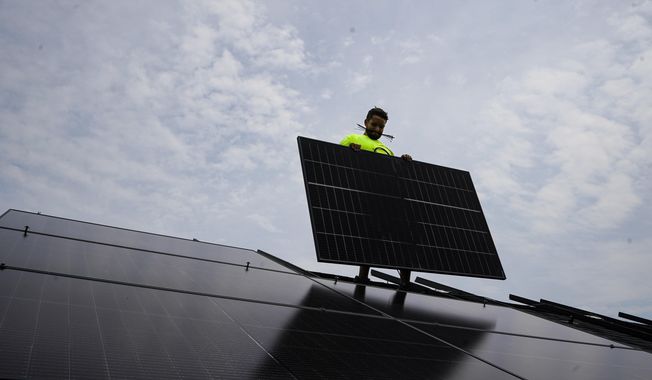 Nicholas Hartnett, owner of Pure Power Solar, holds a panel as his company installs a solar array on the roof of a home in Frankfort, Ky., July 17, 2023. (AP Photo/Michael Conroy, File)