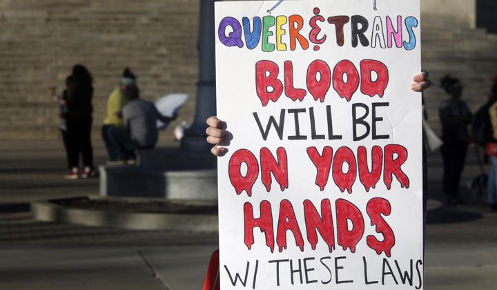 A protester outside the Kansas Statehouse holds a sign after a rally for transgender rights on the Transgender Day of Visibility, March 31, 2023, in Topeka, Kan. A new rule from President Joe Biden&#x27;s administration assuring transgender students be allowed to use the school bathrooms that align with their gender identity could conflict with laws in Republican-controlled states that seek to make sure they can&#x27;t. (AP Photo/John Hanna, File)
