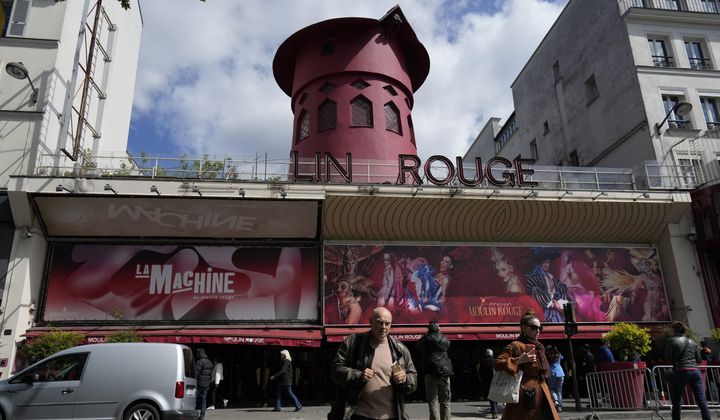 People walk past the Moulin Rouge (Red Mill) Thursday, April 25, 2024 in Paris. The windmill from the Moulin Rouge, the 19th century Parisian cabaret, has fallen off the roof overnight along with some of the letters in its name. (AP Photo/Thibault Camus)