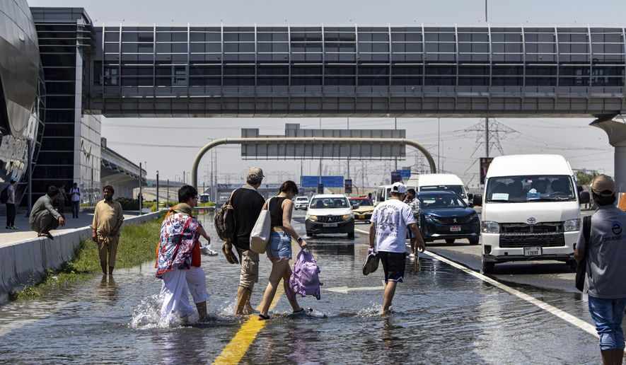 FILE - People walk through floodwater caused by heavy rain while waiting for transportation on Sheikh Zayed Road highway in Dubai, United Arab Emirates, April 18, 2024. A new report says climate change played a role in the floods. (AP Photo/Christopher Pike, File)