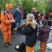 An orange-clad man applauds for a girl playing violin as his orange-clad dog, bottom right corner, runs off during King&#x27;s Day celebrations in Amsterdam, Netherlands, Saturday, April 27, 2024. (AP Photo/Peter Dejong)