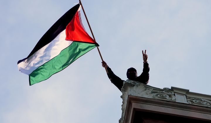 A student protester waves a Palestinian flag above Hamilton Hall on the campus of Columbia University, Tuesday, April 30, 2024, in New York. Early Tuesday, dozens of protesters took over Hamilton Hall, locking arms and carrying furniture and metal barricades to the building. Columbia responded by restricting access to campus. (Pool Photo/Mary Altaffer)