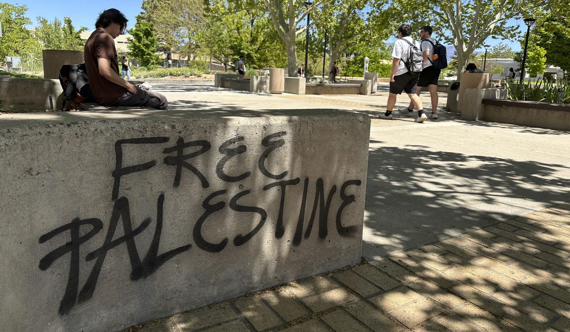 Students walk by one of the spray-painted messages left by those protesting the Israel-Hamas war on the University of New Mexico campus in Albuquerque, New Mexico, Wednesday, May 1, 2024. Sixteen people, including five students, were arrested earlier this week when they occupied the Student Union Building, causing damage inside. (AP Photo/Susan Montoya Bryan)