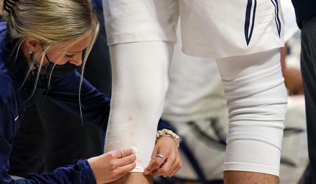A trainer cleans blood off of the uniform of Xavier forward Jack Nunge (24) during the second half of an NCAA college basketball game against Butler, Wednesday, Feb. 2, 2022, in Cincinnati. Colleges and universities are having a difficult time hiring, recruiting and retaining members of their athletic training staffs because of a number of below-market conditions, a survey shows. (AP Photo/Jeff Dean, File)