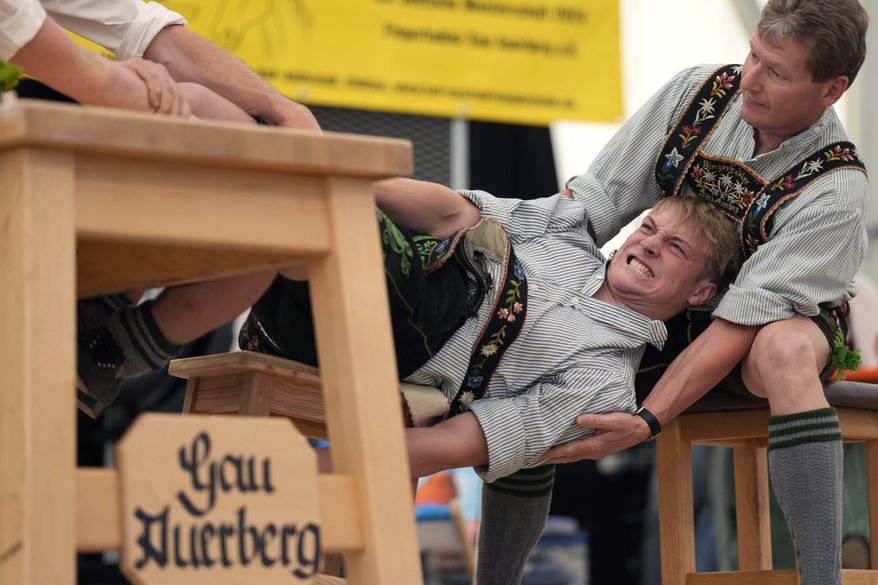 A man dressed in traditional clothes tries to pull his opponent over the table at the German Championships in Fingerhakeln or finger wrestling, in Bernbeuren, Germany, Sunday, May 12, 2024. Competitors battled for the title in this traditional rural sport where the winner has to pull his opponent over a marked line on the table. (AP Photo/Matthias Schrader)