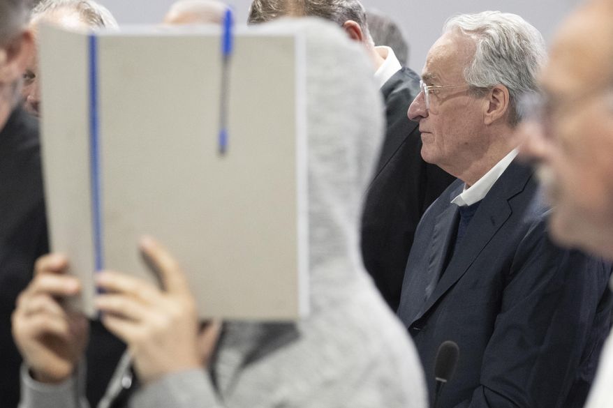 Main defendant Heinrich XIII Prince Reuss, right, stands between his defence lawyers while another defendant hides her face behind a file folder, during a trial against the alleged leaders of a suspected German far-right coup plot, in the Sossenheim branch of the Frankfurt Higher Regional Court, in Frankfurt, Germany, Tuesday, May 21, 2024. The alleged leaders of a suspected far-right plot to topple the German government went on trial on Tuesday, opening the most prominent proceedings in a case that shocked the country in late 2022. Nine defendants faced judges at a special warehouse-like courthouse built on the outskirts of Frankfurt to accommodate the large number of defendants, lawyers and media dealing with the case. (Boris Roessler/Pool Photo via AP)