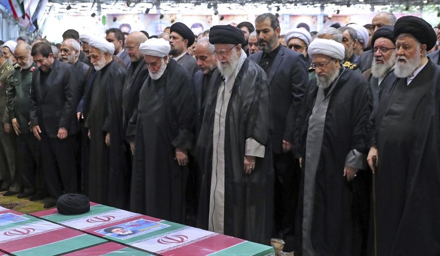 In this photo released by the office of the Iranian supreme leader, Supreme Leader Ayatollah Ali Khamenei, center with black turban, leads a prayer over the flag-draped coffins of the late President Ebrahim Raisi and his companions who were killed in a helicopter crash on Sunday in a mountainous region of the country's northwest, at the Tehran University campus, during a funeral ceremony for them in Tehran, Iran, Wednesday, May 22, 2024. (Office of the Iranian Supreme Leader via AP)