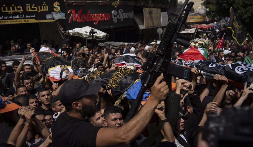 A gunman holds up his weapon as mourners carry the bodies of Palestinians, some draped in the Islamic Jihad militant group flags, during their funeral in the West Bank city of Jenin, Thursday, May 23, 2024. The Israeli military said Thursday it has completed a two-day operation in the occupied West Bank that the Palestinian Health Ministry says killed 12 Palestinians. Militant groups claimed at least eight of the dead as fighters, one from Hamas and seven from the Al-Aqsa Martyrs Brigade. (AP Photo/Leo Correa)
