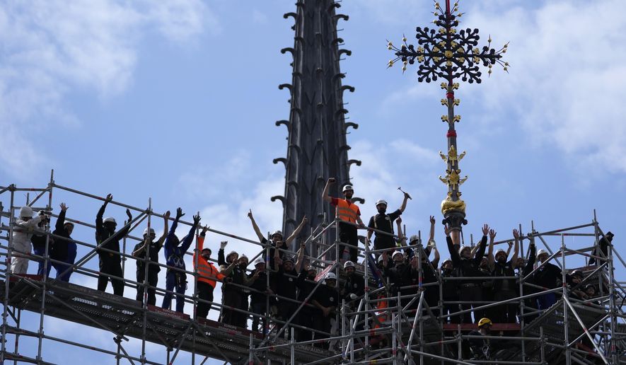 Workers celebrate after reinstalling the Notre Dame de Paris cathedral's Croix du Chevet, right, Friday, May 24, 2024, in Paris. The Croix du Chevet is the only piece of the cathedral roof that did not burn in the devastating April 2019 fire. (AP Photo/Thibault Camus)