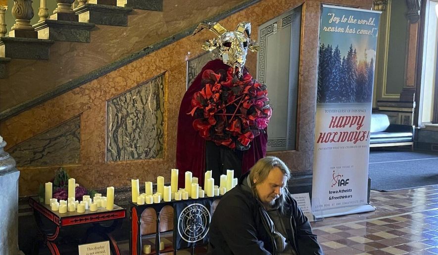 A man prays in Latin in front of a display installed by Satanic Temple Iowa at the Iowa State Capitol in Des Moines, Iowa, on Tuesday, Dec. 12, 2023. A Mississippi man accused of destroying a statue of the pagan idol Baphomet at Iowa's state Capitol pleaded guilty Friday to a reduced charge in return for prosecutors dropping a felony hate crime count. (Caleb McCullough/The Gazette via AP, file)