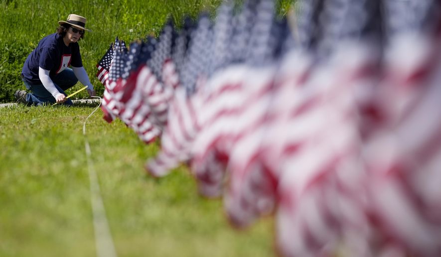 A volunteer helps put up a field of flags near the War Memorial Thursday, May 23, 2024, in Milwaukee. The Memorial Day tribute will feature 27,316 American flags representing Wisconsin residents who paid the ultimate price for freedom in service to our nation. (AP Photo/Morry Gash)