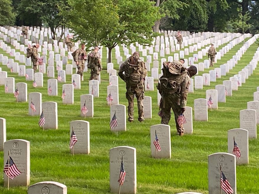 Members of the 3rd Infantry Regiment, known as The Old Guard, place flags at the gravesites at Arlington National Cemetery on Wednesday, May 22, 2024, in preparation for Memorial Day and to honor the U.S. service members buried there. (Mike Glenn/The Washington Times)