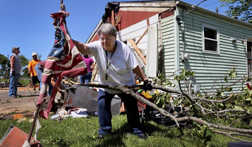 Patti Manley, 69, moves a shredded American flag as she gathers branches from the backyard of her mother's home on Morningdale Place in Mehlville, Mo. on Monday, May 27, 2024, following a violent storm and possible tornado Sunday evening. Manley was staying with her mother Jackie Moloney, 88, when the storm hit. She and her mother rode it out in an interior bathroom. (Robert Cohen/St. Louis Post-Dispatch via AP)