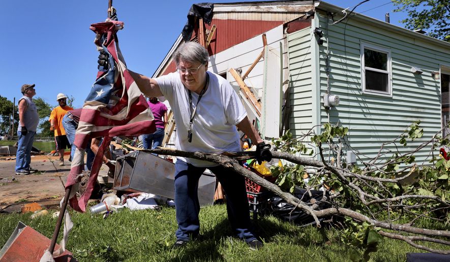 Patti Manley, 69, moves a shredded American flag as she gathers branches from the backyard of her mother's home on Morningdale Place in Mehlville, Mo. on Monday, May 27, 2024, following a violent storm and possible tornado Sunday evening. Manley was staying with her mother Jackie Moloney, 88, when the storm hit. She and her mother rode it out in an interior bathroom. (Robert Cohen/St. Louis Post-Dispatch via AP)