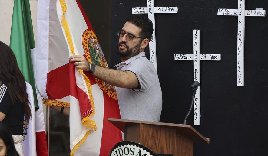 A flag is unfurled in front of the Mexican Consulate in Orlando, Fla., Tuesday, May 21, 2024, for a vigil honoring the eight Mexican farmworkers who were killed in a bus crash last week in Marion County. (Stephen M. Dowell/Orlando Sentinel via AP)