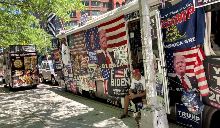 Rocky Granata sits in the doorway of his bus, Friday, May 24, 2024, in New York. Granata and his wife who lived in and sold pro-Donald Trump merchandise out of the bus covered with pro-Trump flags and posters are homeless after the vehicle crashed into several street signs and utility poles on Sunday, June 2. (AP Photo/Karen Matthews)