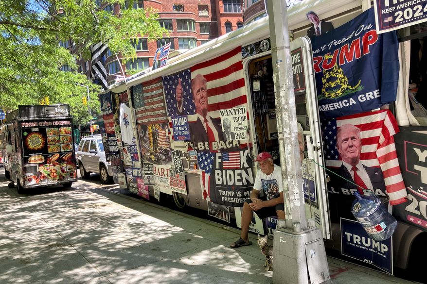 Rocky Granata sits in the doorway of his bus, Friday, May 24, 2024, in New York. Granata and his wife who lived in and sold pro-Donald Trump merchandise out of the bus covered with pro-Trump flags and posters are homeless after the vehicle crashed into several street signs and utility poles on Sunday, June 2. (AP Photo/Karen Matthews)