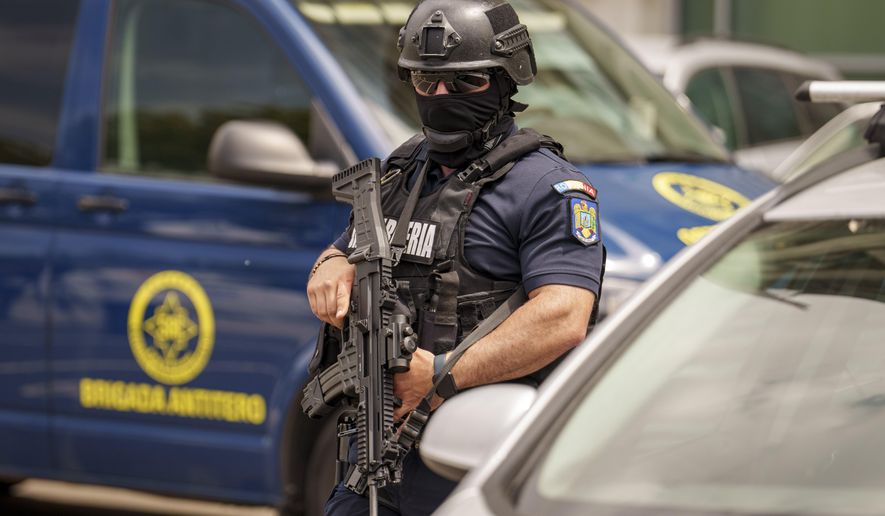 A member of a special unit of the Romanian gendarmerie walks by a van of the anti-terrorist unit of the Romanian Intelligence Service (SRI) outside the apartment block in which the Israeli embassy is located in Bucharest, Romania, Monday, June 3, 2024. A foreign citizen was detained in Romania's capital on Monday after allegedly attacking the entrance of the Israeli Embassy with a Molotov cocktail, causing a small fire but no casualties, local media and police reported. (AP Photo/Vadim Ghirda)