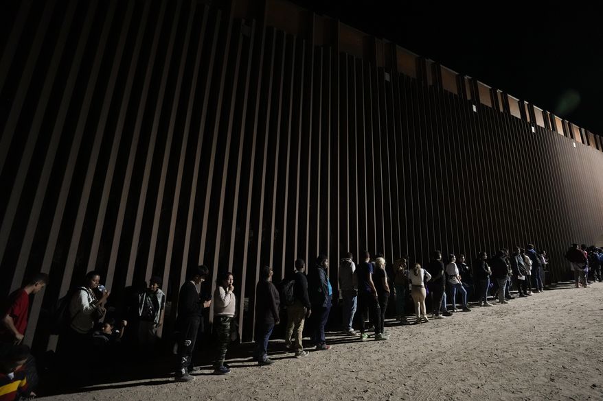 FILE - People line up against a border wall as they wait to apply for asylum after crossing the border from Mexico, July 11, 2023, near Yuma, Ariz. Arizona lawmakers are expected to take a final vote Tuesday, June 4, 2024, on a proposal that would ask voters to make it a state crime for noncitizens to enter the state through Mexico at any location other than a port of entry. (AP Photo/Gregory Bull)