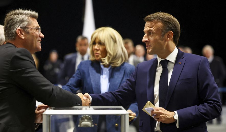 French President Emmanuel Macron, right, shakes hands with a polling station official during the European election, Sunday, June 9, 2024 in Le Touquet-Paris-Plage, northern France. Polling stations opened across Europe on Sunday as voters from 20 countries cast ballots in elections that are expected to shift the European Union's parliament to the right and could reshape the future direction of the world's biggest trading bloc. (Hannah McKay/Pool via AP)