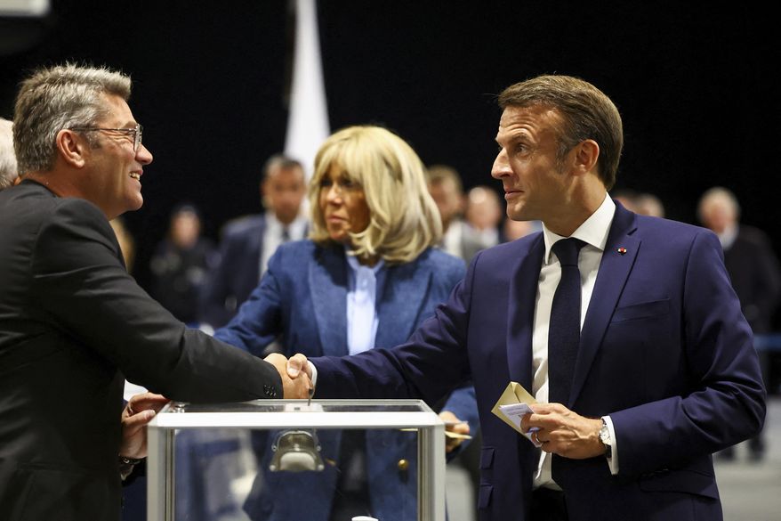 French President Emmanuel Macron, right, shakes hands with a polling station official during the European election, Sunday, June 9, 2024 in Le Touquet-Paris-Plage, northern France. Polling stations opened across Europe on Sunday as voters from 20 countries cast ballots in elections that are expected to shift the European Union's parliament to the right and could reshape the future direction of the world's biggest trading bloc. (Hannah McKay/Pool via AP)
