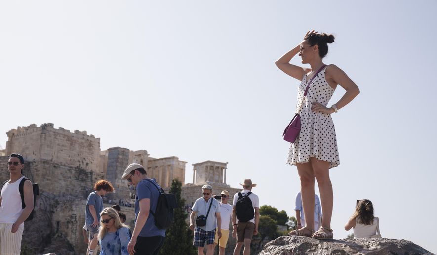 Tourists stand at the Aeropagous hill in front of the ancient Acropolis, in central Athens on Wednesday, June 12, 2024. The ancient site of Acropolis will be closed to the public for five hours due to a heat wave that pushed temperatures to 39 degrees Celsius (102 Fahrenheit) in the capital and even higher in parts of central Greece. (AP Photo/Petros Giannakouris)