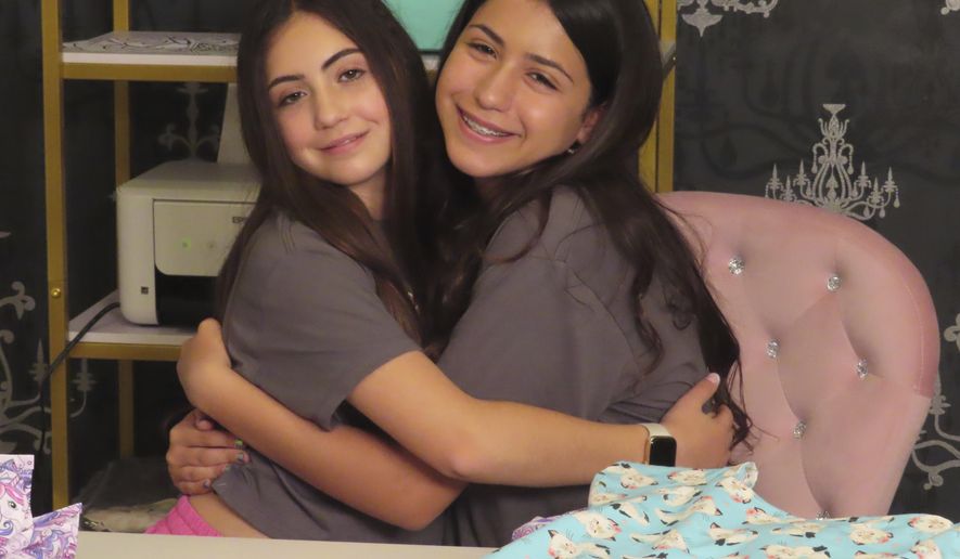 Audrina Demma, left, and her sister Giuliana hug in the basement at the sewing station of their Freehold, N.J., home on June 19, 2024. The sisters have sewn and donated 1,800 hospital gowns to sick children in 36 states plus Africa. Giuliana was inspired by seeing her baby cousin wearing an ugly, ill-fitting gown while hospitalized with brain cancer in 2017. (AP Photo/Wayne Parry)