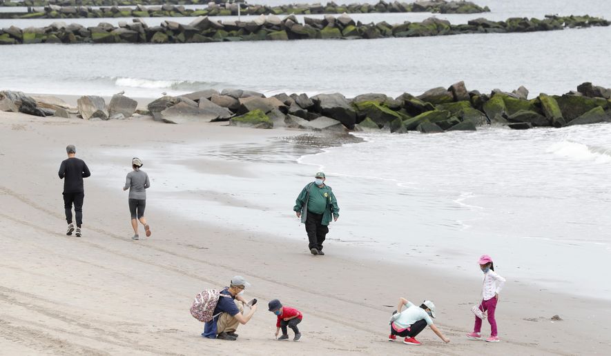 Children play in the sand while others jog as a New York City Parks officer, center, walks the beach making sure no one goes in the water, at Coney Island Beach during the current coronavirus outbreak, on May 24, 2020, in New York. Police in New York said two teenagers died while swimming at Coney Island Beach in Brooklyn, a news report said. (AP Photo/Kathy Willens, File)