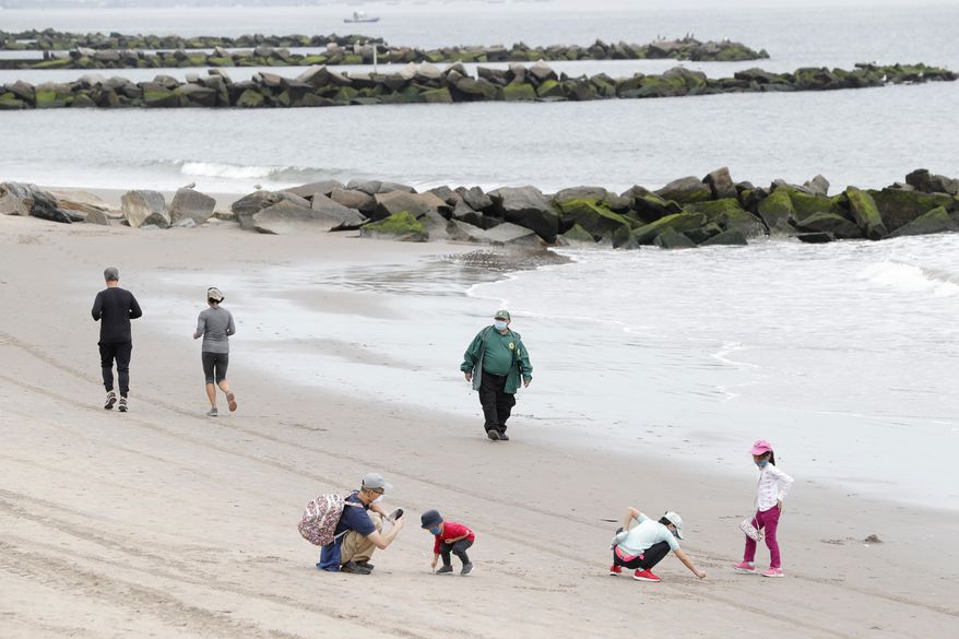 Children play in the sand while others jog as a New York City Parks officer, center, walks the beach making sure no one goes in the water, at Coney Island Beach during the current coronavirus outbreak, on May 24, 2020, in New York. Police in New York said two teenagers died while swimming at Coney Island Beach in Brooklyn, a news report said. (AP Photo/Kathy Willens, File)