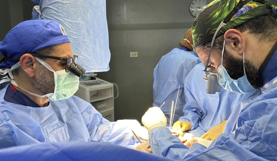 This handout photo taken on May 12, 2023 shows Dr. Adam Hamawy, left, a former U.S. Army combat plastic surgeon who volunteered in Gaza in May and Dr. Mohammed Tahir, a British surgeon, performing surgery on mangled hand from a blast injury at the European General Hospital, in Khan Younis, Gaza. (Adam Hamawy via AP)