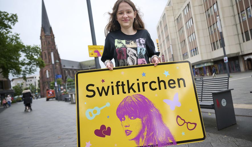 Schoolgirl Aleshanee Westhoff shows a "Swiftkirchen" town sign in honor of musician Taylor Swift in Gelsenkirchen, Germany, Tuesday, July 2, 2024. The German city of Gelsenkirchen, which temporarily put up signs renaming itself “Swiftkirchen” before the American superstar played three concerts there in mid-July, says it received 1,400 bids for the signs from Germany and abroad. (Bernd Thissen/dpa via AP, File)