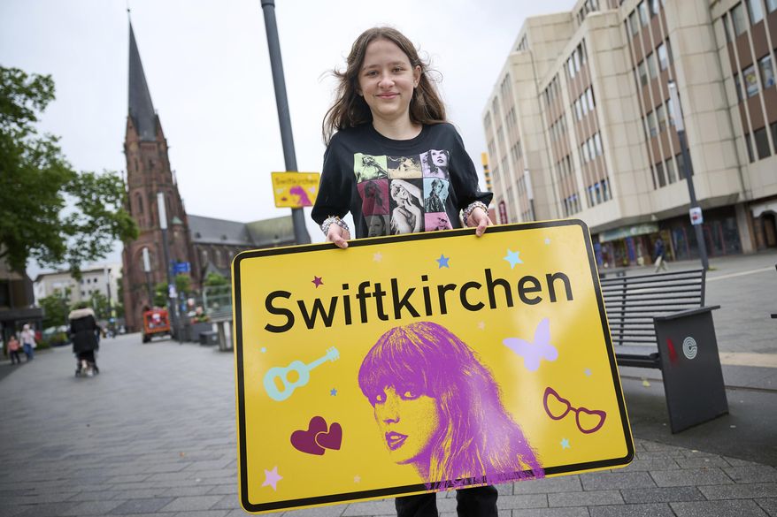 Schoolgirl Aleshanee Westhoff shows a "Swiftkirchen" town sign in honor of musician Taylor Swift in Gelsenkirchen, Germany, Tuesday, July 2, 2024. The German city of Gelsenkirchen, which temporarily put up signs renaming itself “Swiftkirchen” before the American superstar played three concerts there in mid-July, says it received 1,400 bids for the signs from Germany and abroad. (Bernd Thissen/dpa via AP, File)