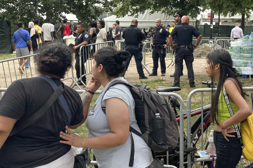 Asylum seekers watch police activity on the migrant shelter at Randall's Island, Friday, Aug. 2, 2024, in New York. Police searched New York City's largest asylum-seeker shelter for hours Friday, saying they were looking for any "dangerous contraband" among its 3,000 residents, many of whom waited outside on a sweltering summer day. (AP Photo/David R. Martin)