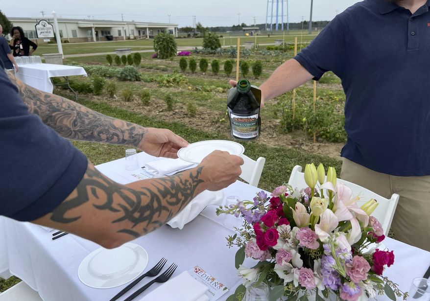 Two incarcerated men pour olive oil on to a plate at a dinner event inside the Grafton Reintegration Center in Grafton, Ohio on Thursday, Aug. 15, 2024. (AP Photo/Patrick Aftoora Orsagos)