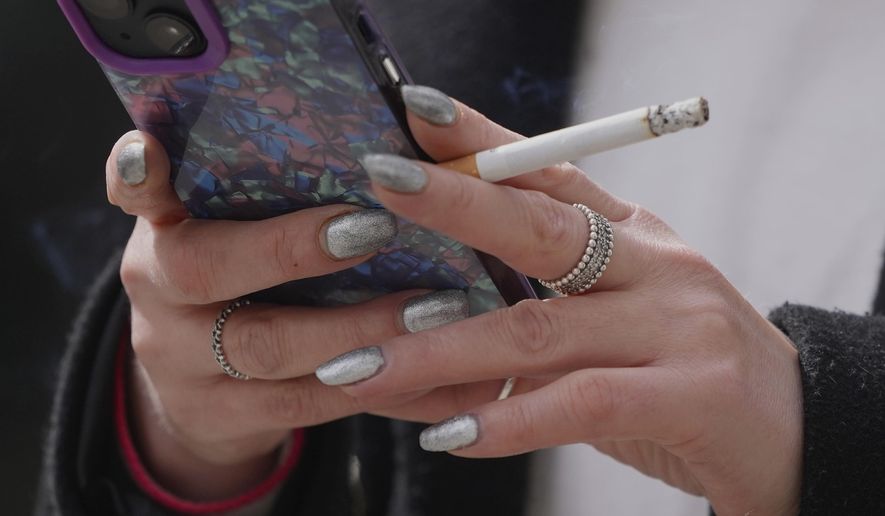 FILE - A woman smokes on a street, in London, on April 16, 2024. (AP Photo/Kin Cheung, File)